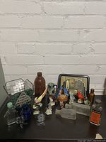 Overview photo showing 21-piece lot of vintage collectibles including birds and bottles on a table against a white brick wall.