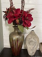 Taller ceramic vase with drip glaze and artificial red flowers alongside smaller textured beige vase