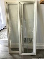 Full view of two tall rectangular cabinet panels leaning against a wall showing wooden frame and clear glass surface.