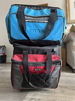 Stacked view of two soft shell coolers, blue Titan Design cooler on top and red Columbia cooler on bottom