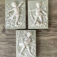 Set of three Arnart jasperware wall plaques laid out showing cherubic figures in white relief on a light green rectangular base.
