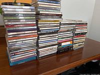 Multiple stacks of CD jewel cases containing over 100 discs visible on a wooden table.