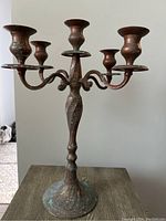 Side view of the copper candelabra showing curved arms and natural green patina.