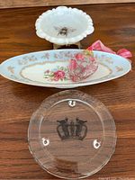 Two porcelain trinket trays and one glass candle stand on wooden surface.