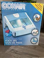 Photo of Conair Ultra Massaging Heated Foot Spa box showing front with product image and features including 3 massage rollers, spiral water jets, and heated water.