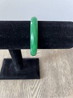 Front view of green jade bangle on black velvet stand to show color and surface finish.