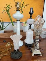 Photo showing all four lamps together on a table, highlighting their size differences, glass lamp bodies, and metal bases.