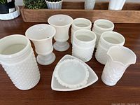Front view of 10 milk glass items on wood surface with varying shapes including glasses, vases, and dishes