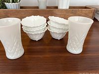 Photo showing 8 small white milk glass relish or dessert cups with scalloped edges and textured ribbing, arranged in two stacks, with two small white milk glass juice glasses with diamond pattern on either side.