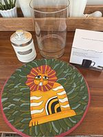 All four items arranged together on wood surface: art plate with lion motif, vintage coffee container, clear glass container, boxed mug set