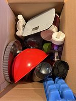 Top view photo showing the contents of a box with various kitchen items including a red mixing bowl, round baking pan, water bottles, and thermoses.