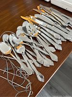 Full set of silver-tone cutlery with ornate handles laid out on wooden surface.
