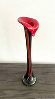 Full view of the Murano glass calla lily vase standing on a dark wooden surface, showing the tall black and red swirled stem with the red flower top.