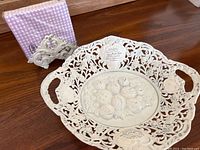 Full view of metal napkin holder with purple checkered napkins and distressed white metal bread basket with fruit motif center and ornate cut-out design