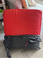 Red outdoor patio couch cushion, front view showing the fabric and condition. Cushion is rectangular and about 24x25x5 inches. Fabric is red, slightly soiled.