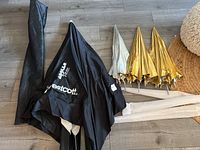 Overview of five umbrellas including folded black Westcott Apollo umbrella and four gold/silver bounce umbrellas lying on wooden floor with protective cases.
