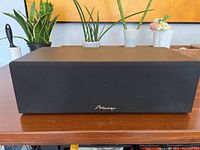 Front view of large rectangular stereo speaker with black fabric grille and wooden top surface.