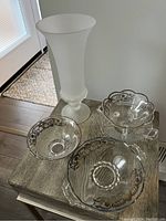 Photo showing the full set of vintage glassware including the frosted glass vase and three clear glass dishes with silver overlay accents on a wooden table.