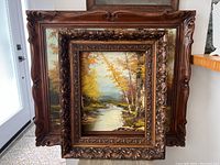 Two vintage wood framed oil paintings stacked against a wall showing the ornate carved wood frames.