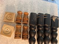 Image showing 4 large black coffee table legs with brass inlay, 4 smaller natural wood couch or chair legs, and 2 of 4 pinewood square decorative pieces with circular recess detail.