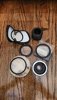 Camera lens attachments laid out on wood surface including lenses, adapter rings and filters in cases.