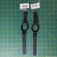 Two black resin Casio G-Shock replacement watch bands with bezels, new with tags, displayed on green cutting mat.