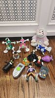 Various early 2000s electronic and character toys arranged on wood floor in front of white wall vent