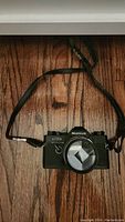 Front view of black Mamiya ML 300s 35mm camera with attached strap on wooden surface.