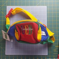 Front view of multicolor fanny pack with UCB Benetton embroidered logo on red pocket with yellow adjustable strap and red buckle.