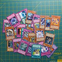 Photo showing a spread of about 29 Yugioh trading cards in different categories (monster, trap, spell) on a green gridded cutting mat.