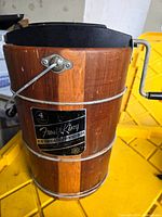 Side view of wooden ice cream bucket with black lid and handle, showing metal bands and hand crank