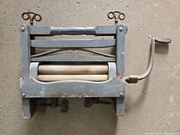 Front view of antique wooden hand crank wringer showing wooden frame, two fabric rollers, and hand crank on the right side.
