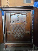 Front view of the antique wooden tube radio showing the cabinet carvings, three knobs, and lower grille with decorative pattern.