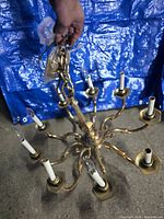 Full view of the bronze chandelier showing eight arms with candle-style light sockets and hanging chain, held up by a hand against a blue tarp background.