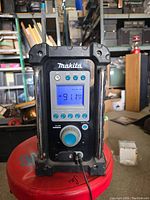 Front view showing the digital screen displaying FM frequency 91.1 MHz, volume knob with blue grip, preset buttons, Makita logo and antenna extended.