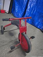 Front angle view of the vintage metal kids tricycle showing large front wheel, pedals and handlebar grips.