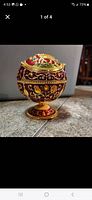 Metal globe-shaped ashtray on pedestal base with red and gold floral decoration.