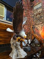 Full side view of the bald eagle statue showing wings spread and perched on a base, set against an interior background with wooden furniture and decor.
