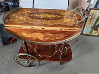 Front angle of the vintage Italian marquetry wood serving bar tea cart with wheels, showing floral inlaid top and brass gallery rail.