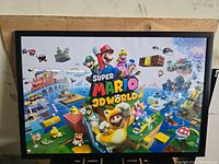 Photo of vintage Super Mario 3D World framed poster hung on wall, shows full artwork and frame.