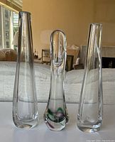 Three tall clear glass vases on a sofa backrest with a living room background.