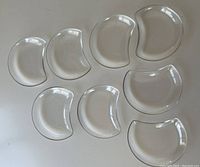 Eight kidney-shaped small clear glass salad plates arranged flat on white surface.