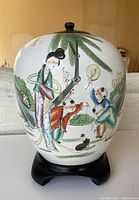 Front view of the antique Chinese porcelain ginger jar showing the detailed hand-painted scene and wooden base.