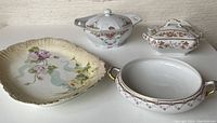 Four antique European serving pieces displayed together, showing hand-painted floral designs on each piece.