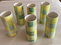 Overview of all six ceramic tall cups arranged on a flat, neutral surface, showing the uniform size and pattern colors.