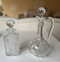 Pair of crystal decanters shown on white surface with soft background - clear glass with intricate geometric and starburst cut patterns.