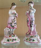 View of both porcelain figurines together showing delicate paint and floral details.