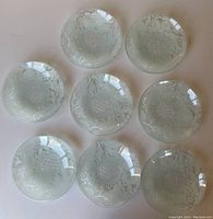 Top view of 8 frosted green glass dessert plates featuring pineapple and floral motifs arranged in a circle.