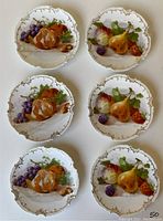 Close-up of 6 porcelain dessert plates showing two different fruit motif designs with vibrant colors on decorative scalloped edges.