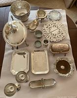 Overview of the silver plated serving pieces laid out on a table, including trays, bowls, chafing dish, goblets, and other assorted pieces.